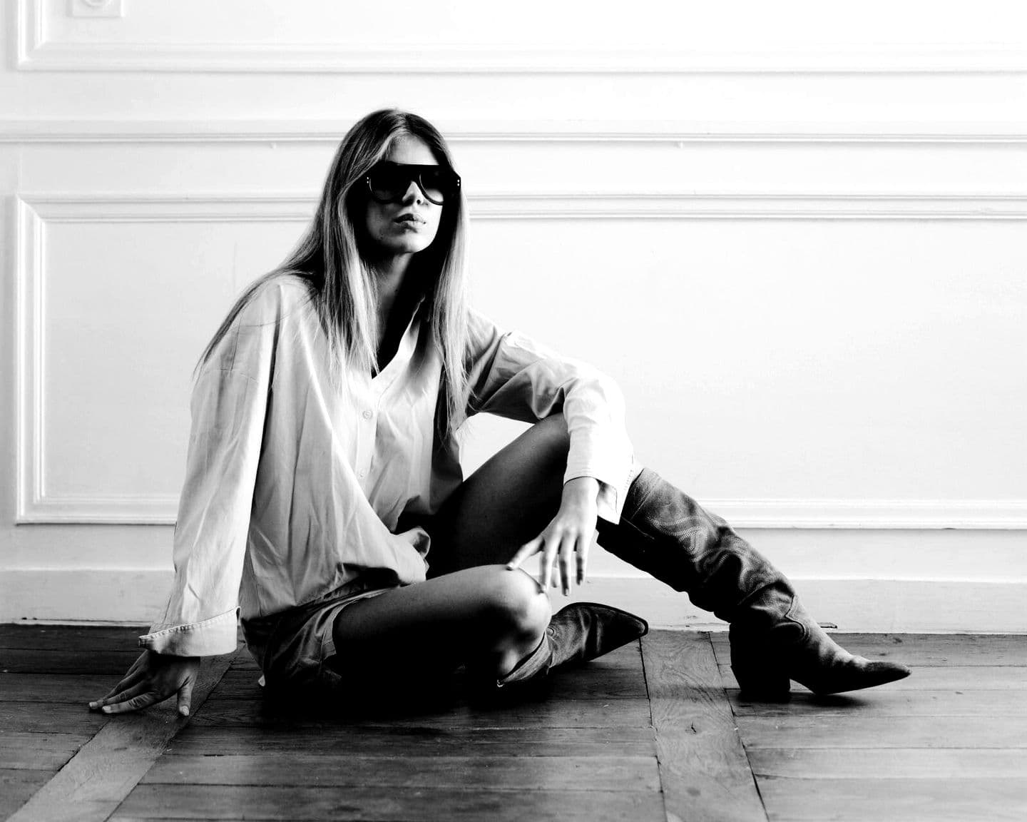 MYKANA seated on a parquet floor in sunglasses